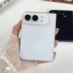 iPhone Ultra: Apple’s First Foldable Phone Rumored Specs 4 Hand holding a white iPhone Ultra foldable phone shown from the back, featuring dual camera lenses in a rounded module, with a black unit placed beside it on a plain white surface