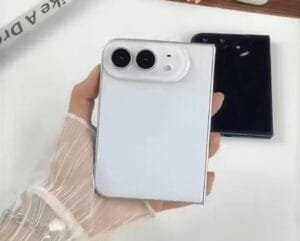 Hand holding a white iPhone Ultra foldable phone shown from the back, featuring dual camera lenses in a rounded module, with a black unit placed beside it on a plain white surface