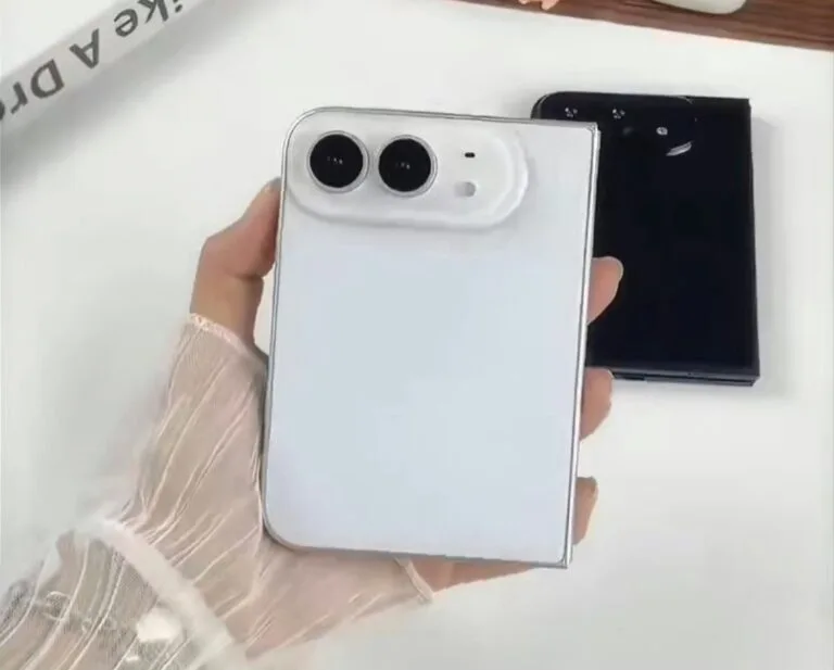Hand holding a white iPhone Ultra foldable phone shown from the back, featuring dual camera lenses in a rounded module, with a black unit placed beside it on a plain white surface