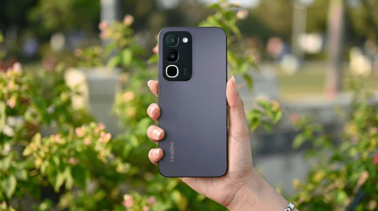 Back view of the Realme P4R 5G in matte dark finish, held in hand against soft green outdoor background; triple‑camera module visible at the top left, with vertical Realme branding near the bottom.