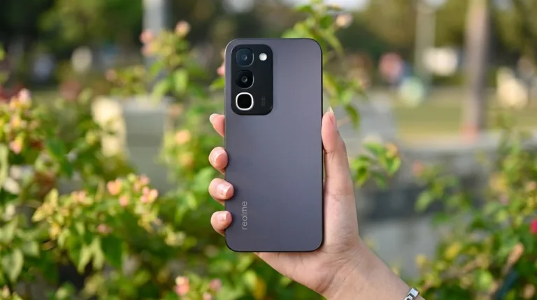 Back view of the Realme P4R 5G in matte dark finish, held in hand against soft green outdoor background; triple‑camera module visible at the top left, with vertical Realme branding near the bottom.