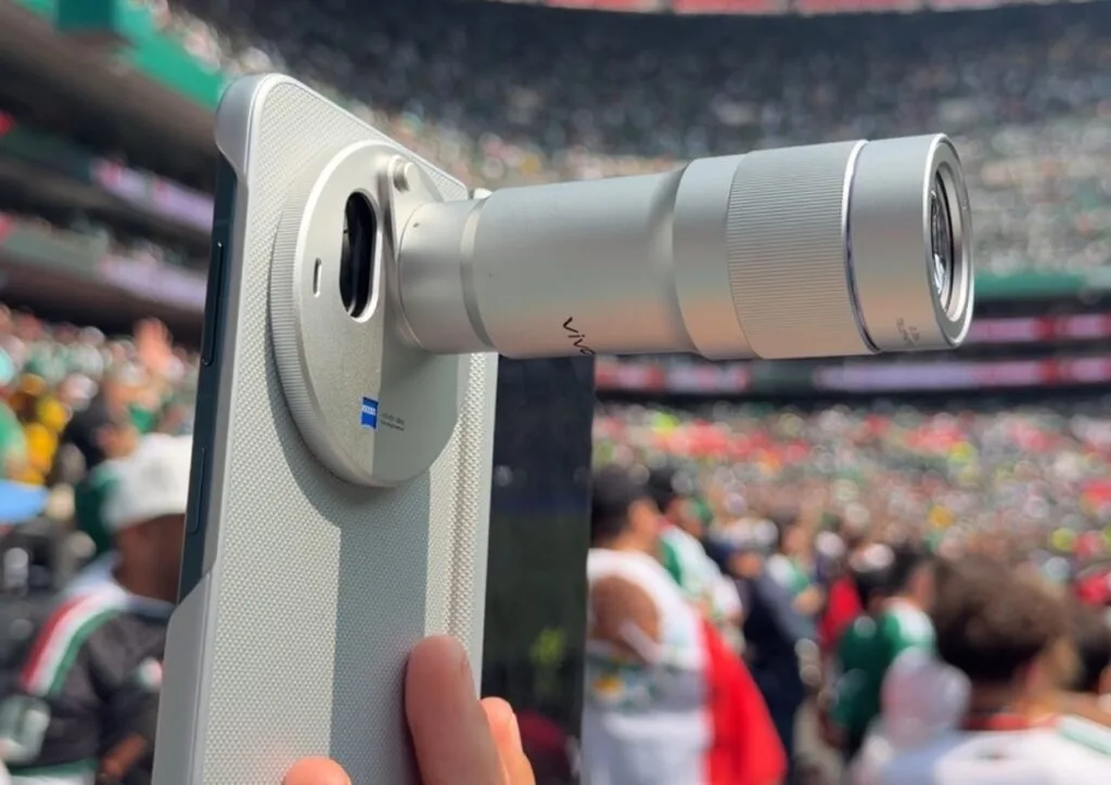 Vivo X Fold 6 Camera Specifications Revealed Vivo X Fold 6 foldable smartphone with extended telephoto lens accessory, ZEISS certified camera system, light textured rear panel, captured at stadium event for long distance shooting.