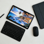 Tecno Mega PAD 2 laid flat on a plain white surface, paired with a matching Bluetooth keyboard, protective case, wireless mouse, and stylus pen. The tablet displays a vivid scenic wallpaper, highlighting its sleek design and full accessory bundle.