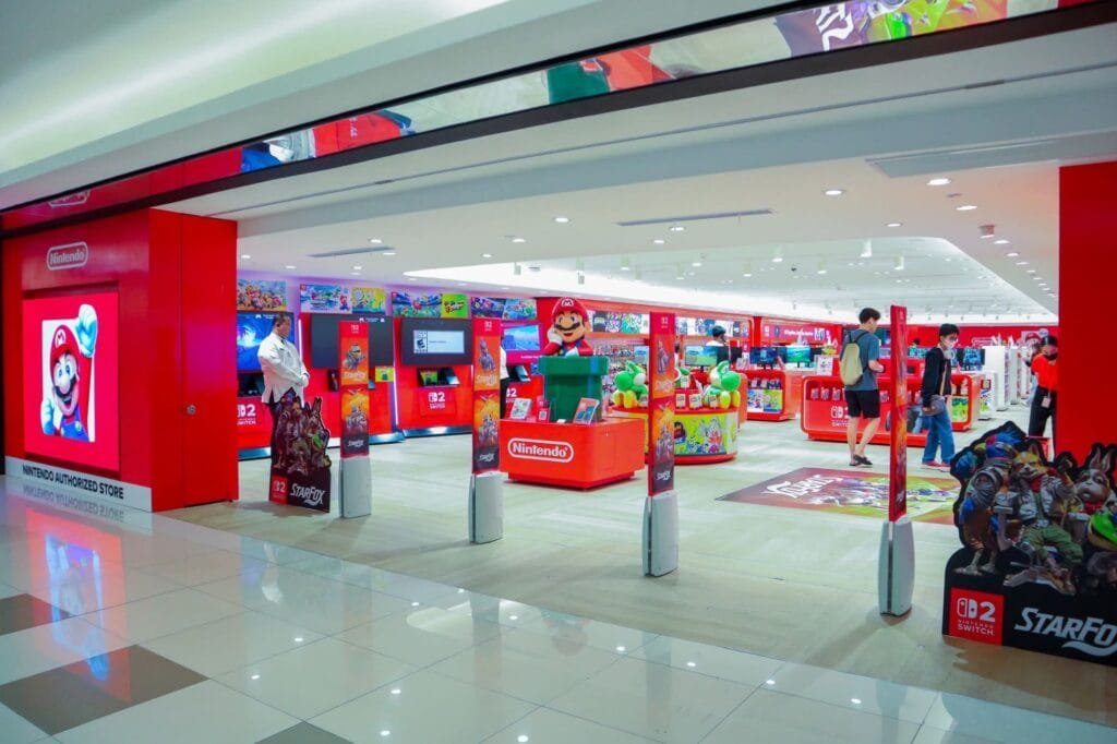 Rhythm Heaven Groove Officially Announced for Nintendo Switch 2 in the Philippines 1 Entrance and interior of the official Nintendo Authorized Store at SM Makati Ayala Center. The bright red storefront displays the Nintendo logo and a large Mario graphic. Inside, red display fixtures showcase Nintendo Switch games and merchandise, with prominent promotional stands for Star Fox and other titles. A Mario statue stands near the center, while visitors browse products across the well lit, spacious retail space.