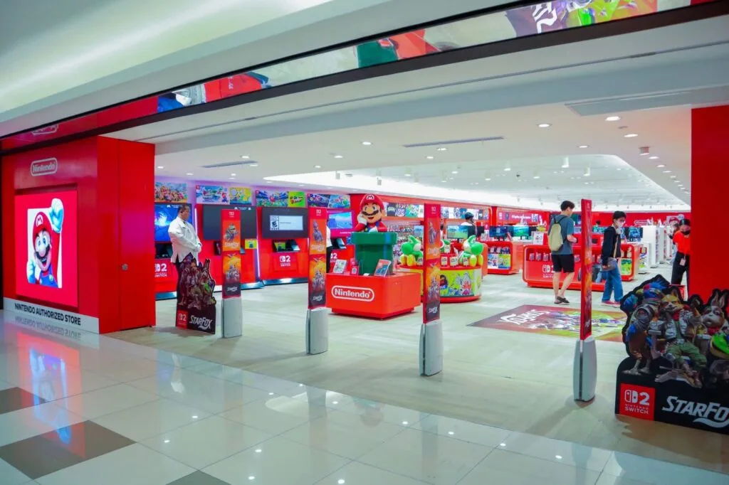 Rhythm Heaven Groove Officially Announced for Nintendo Switch 2 in the Philippines 1 Entrance and interior of the official Nintendo Authorized Store at SM Makati Ayala Center. The bright red storefront displays the Nintendo logo and a large Mario graphic. Inside, red display fixtures showcase Nintendo Switch games and merchandise, with prominent promotional stands for Star Fox and other titles. A Mario statue stands near the center, while visitors browse products across the well lit, spacious retail space.