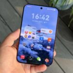 Huawei Pura X View smartphone held in hand. Front view showing large wide screen display, slim rounded edges, and premium finish. Home screen with HarmonyOS interface, time and date, and app icons including WeChat, Douyin, and Xiaohongshu. Soft outdoor background.