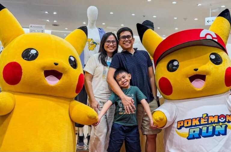 Family posing with two large Pikachu mascots at Pokémon 30th anniversary event at SM Mall of Asia. One Pikachu wears a red cap and a Pokémon Run shirt