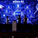 DICT Adds Free AI Assistant to eGovPH App, Now Serving 61 Million Filipinos 1 eGovAI launch event at The Manila Hotel, large digital screen displaying features including Identity AI and Document Extractor, Philippine flag on left, three silhouettes on stage