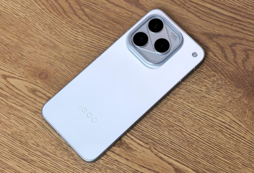 iQOO 16 Launched in China with Snapdragon 8 Elite Extreme Gen 6, Triple 50MP Cameras, and 8,400mAh Battery iQOO 16 in white finish showing triangular triple camera module with 100X zoom marking on wood surface