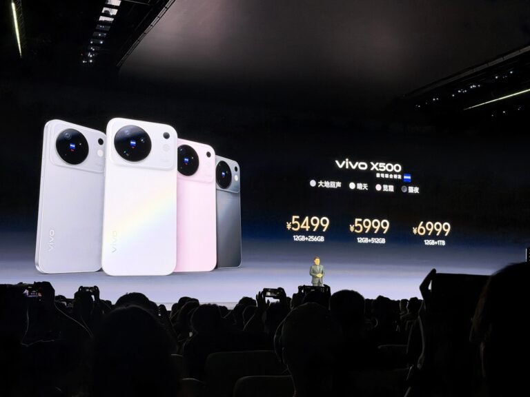 Vivo X500 launch event showing four color variants on stage screen with pricing 5499 to 6999 CNY, presenter standing below, audience taking photos