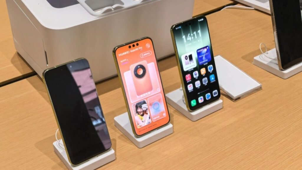 Huawei’s Mate 90 and Mate 90 Pro Hit China With New Chips, Cameras, and HarmonyOS 7 Huawei Mate 90 and Mate 90 Pro displayed side by side on white stands at an official showcase, showing front views with gold frames and the Mate 90 Pro displaying the Ruiying Z10 camera module pairing screen