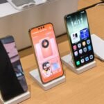 Huawei’s Mate 90 and Mate 90 Pro Hit China With New Chips, Cameras, and HarmonyOS 7 2 Huawei Mate 90 and Mate 90 Pro displayed side by side on white stands at an official showcase, showing front views with gold frames and the Mate 90 Pro displaying the Ruiying Z10 camera module pairing screen