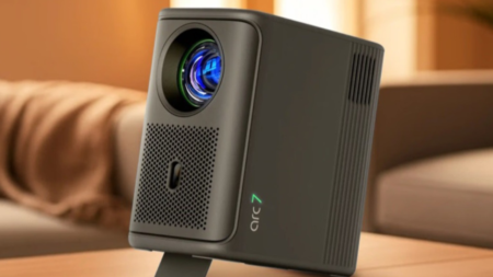 Lumio Arc 7 (2026 edition) compact matte grey projector on wooden table in living room, showing illuminated lens and Arc 7 branding