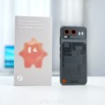STEPX Neo Is The First Phone Built Around A Native AI Agent 1 StepX Neo rear view in dark gray translucent finish showing circuit pattern design dual orange-ring camera lenses next to white retail box with orange star mascot
