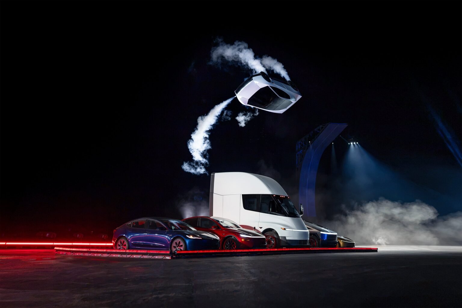 Tesla Unveils Thruster-Powered Roadster 2, Targets 2028 Production Tesla Roadster 2 performing a mid air flip above a lineup including Model 3 Model Y Semi and Cybertruck with cold gas thrusters firing.